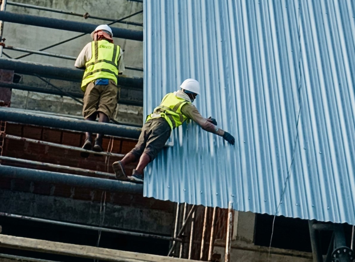 Workers installing blue aluminium roofing panels on scaffolding